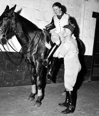 29 Oct 1954, New York, New York, USA --- Mrs. Lis Hartel, Danish horsewoman who is the 1954 world's champion dressage champion in both the men's and women's classes, is shown her during a practice session at Squadron Armory in New York for her appearance in the 66th National Horse Show at Madison Square Garden, November 2-9. Mrs. Hartel, who was stricken with polio in 1944 must still be helped into and out of the saddle. Photo shows Mrs. Hartel being helped to dismount by her groom. --- Image by © Bettmann/CORBIS
